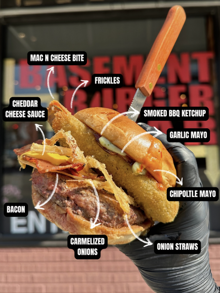 Loaded burger from Basement Burger Bar with mac n cheese bites, fried pickles, smoked bbq ketchup, garlic mayo, chipotle mayo, cheddar cheese sauce, and bacon 