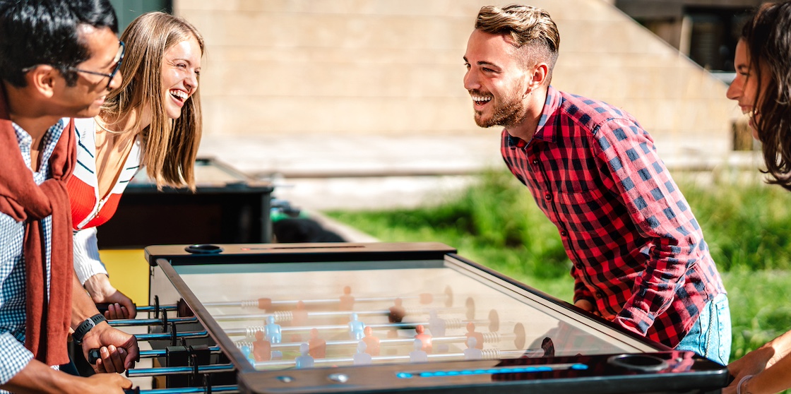 friends play kicker table foosball at open space bar -Friendship life style concept with happy millennial having fun together at garden party - Bright warm filter with focus on right guy friends with competitive activites