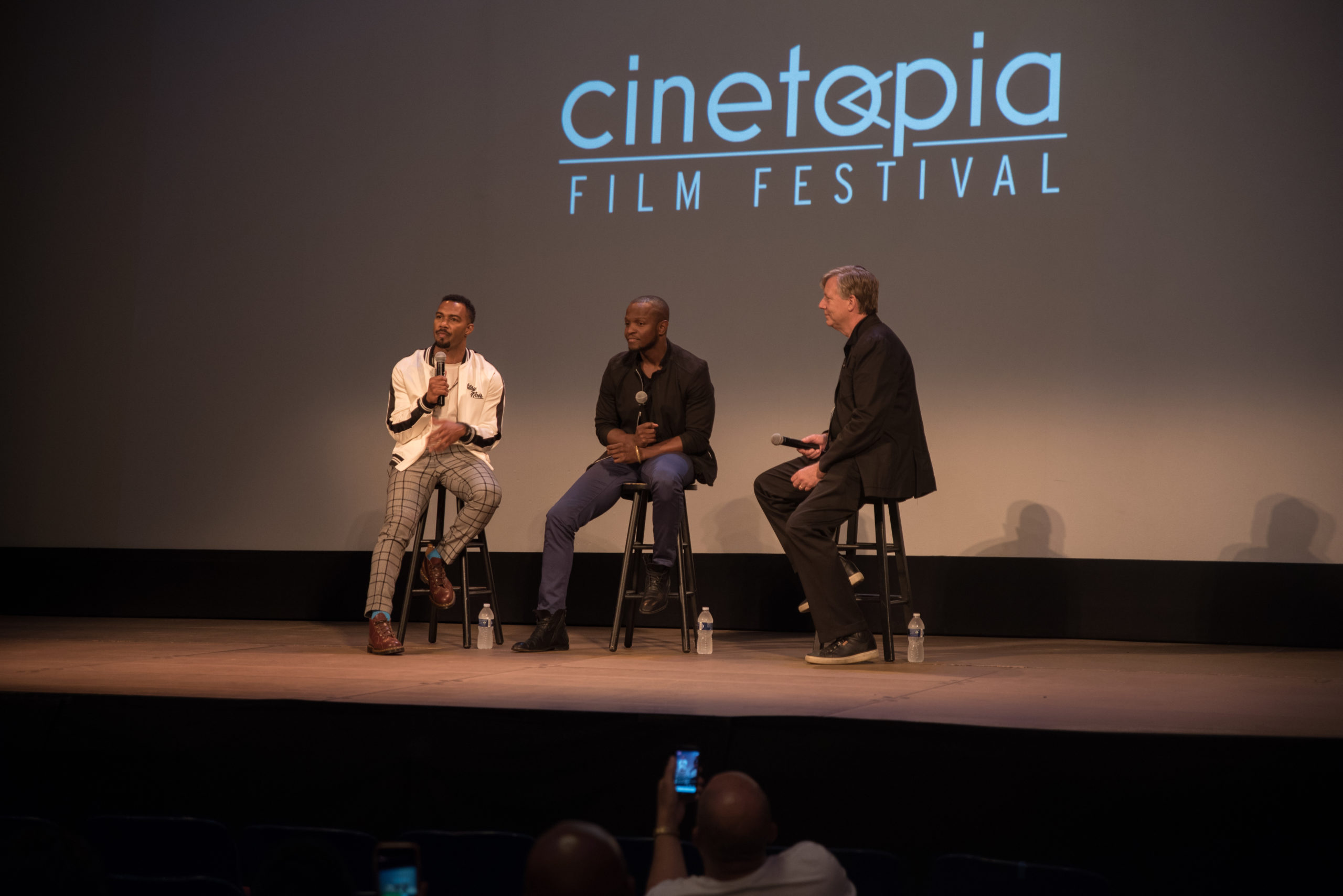 Three men on stage at film festival, having a panel conversation