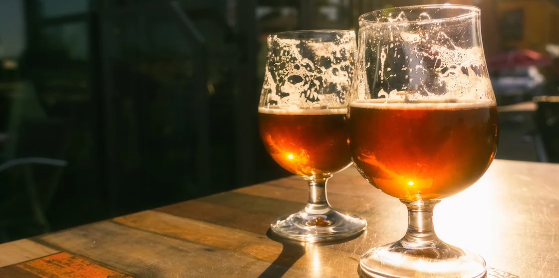 Closeup of two glasses of beer on terrace table with evening sun shining through them. Relaxation, food and drink concept with copy space.