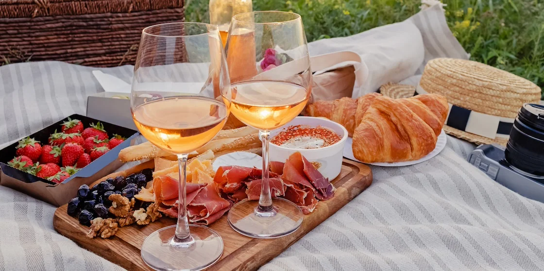 Delicious picnic with strawberries, croissants and appetizers on the board and rose wine. Beautiful sunset light near the sea at sunny summer day for al fresco dining