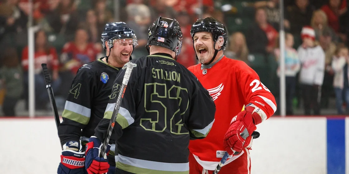 two Michigan Warrior players laughing with a Red Wings Alum on the ice