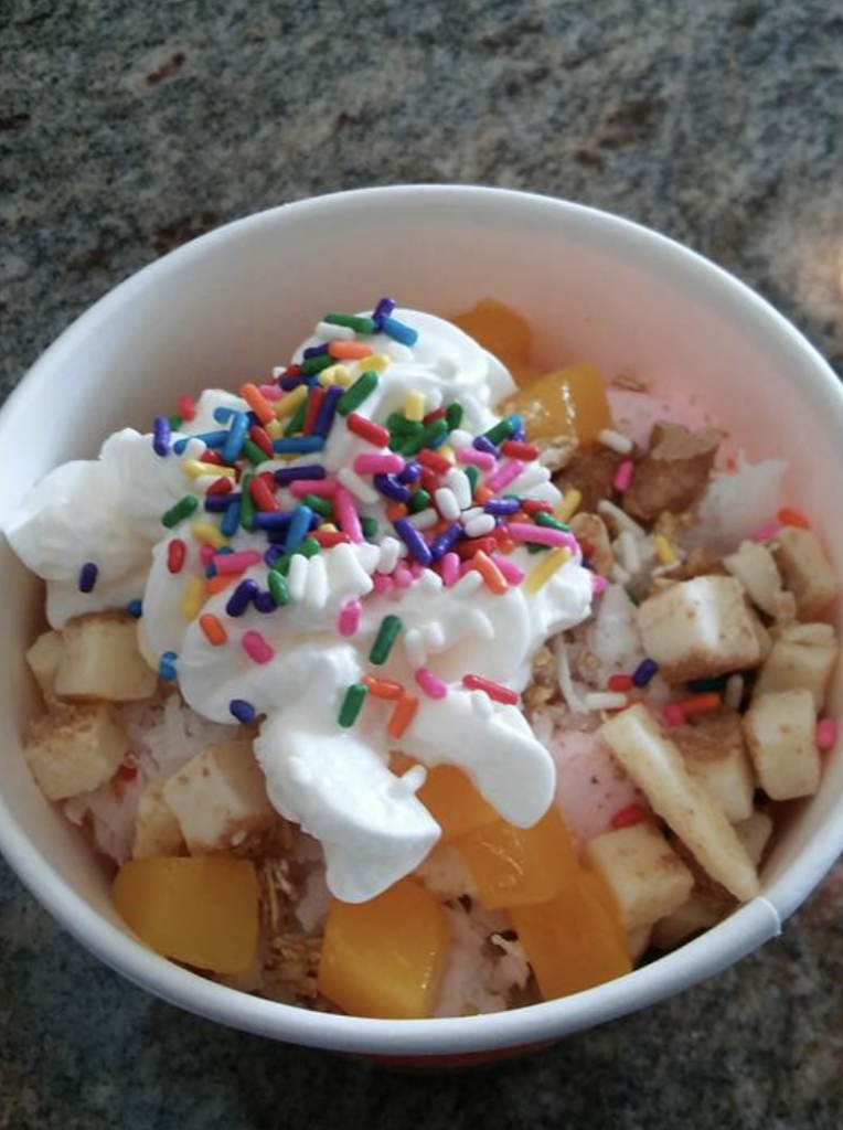 Sweet Island Yogurt topped with whipped cream, sprinkles, fruit, and cheesecake bites
