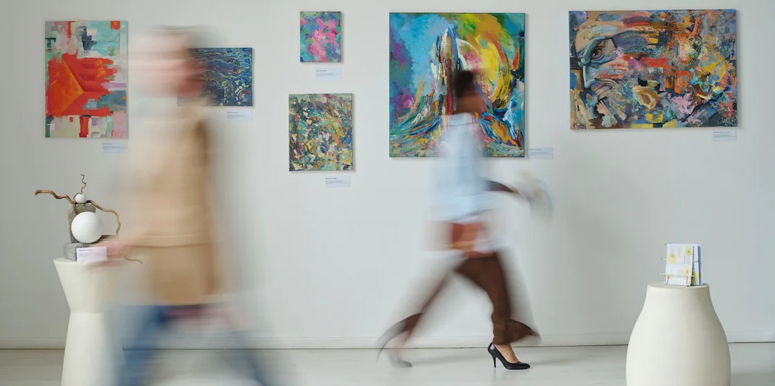 Blurred motion of people passing through the paintings on the wall in art gallery