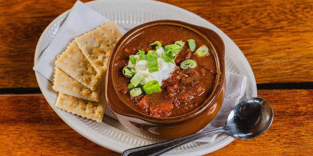 a bowl of chili topped with scallions and sour cream, with crackers on the side from Camp Ticonderoga