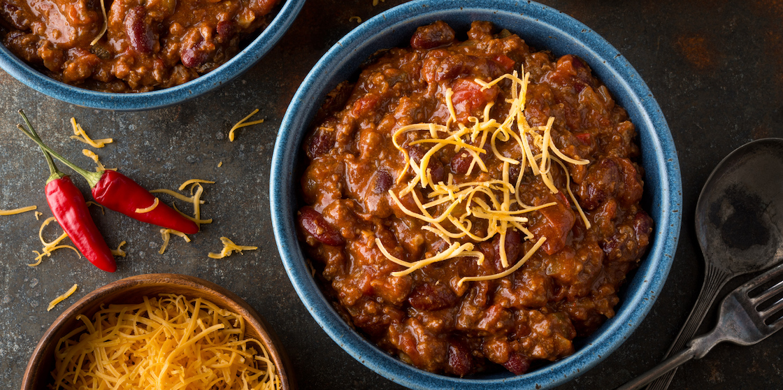 A bowl of chili with ground beef, kidney beans, red pepper, tomato and shredded cheddar cheese.
