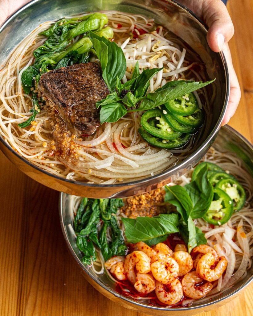 two bowls of noodles from ima, including steak, shrimp, peppers, basil, and other spices