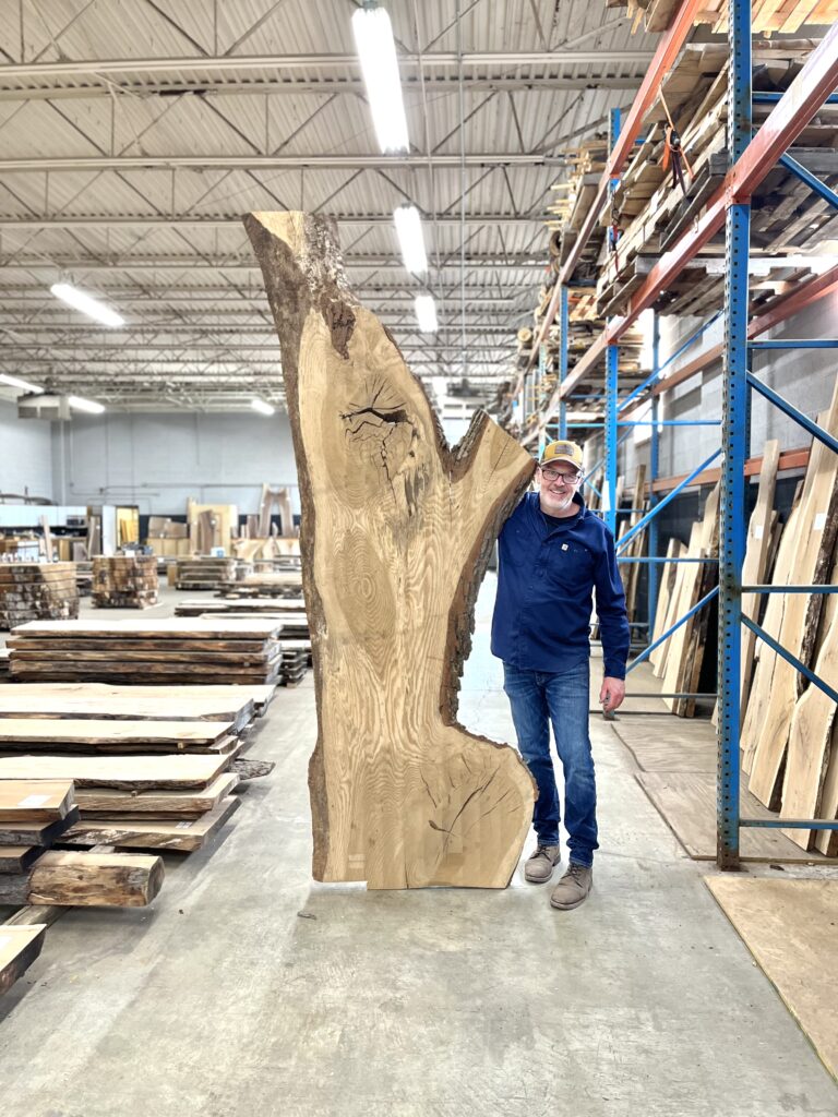 owner of live edge detroit standing with a large slab of wood inside the warehouse