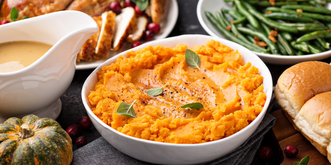 Mashed sweet potatoes with butter and cinnamon on Thanksgiving table with sides of turkey and green beans