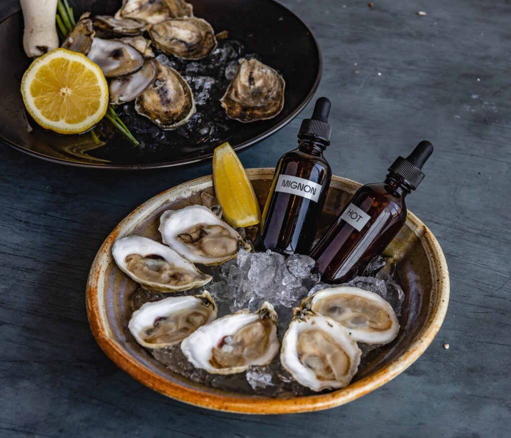 bowls of raw oysters on ice with lemon and bottles of sauce from bar pigalle