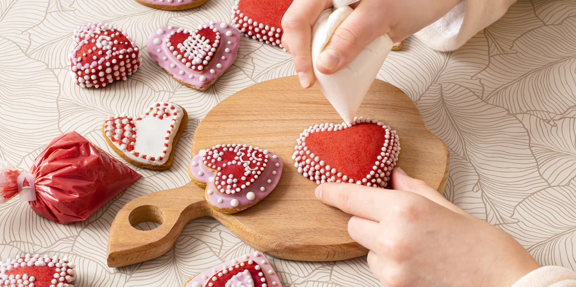 Girl's hands apply icing from pastry bag to handmade gingerbread cookies. Heart shaped gingerbread for Valentine's Day. Pastry craft and art
