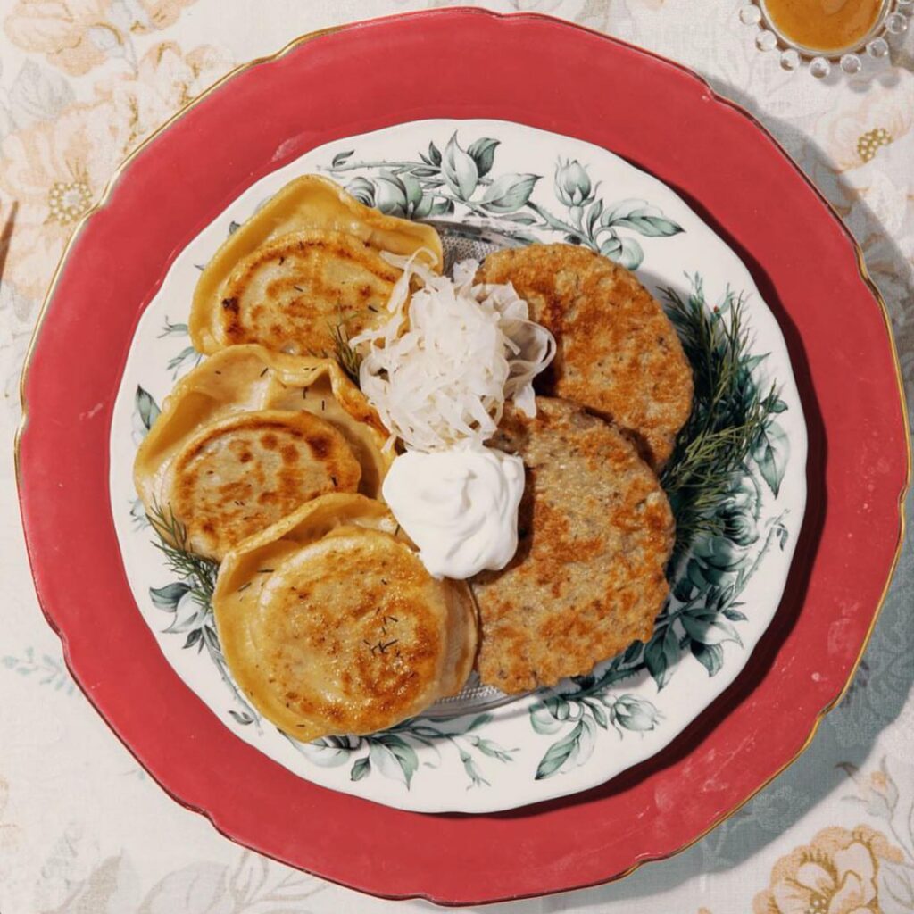 plate of pierogi and potato pancakes with sour cream and kraut on floral and red plate - polish cuisine