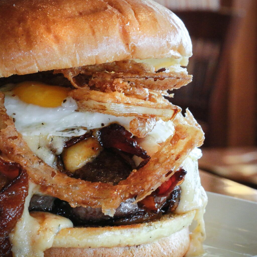 burger with cheese, onion strings, an egg, and more from stillwater grill