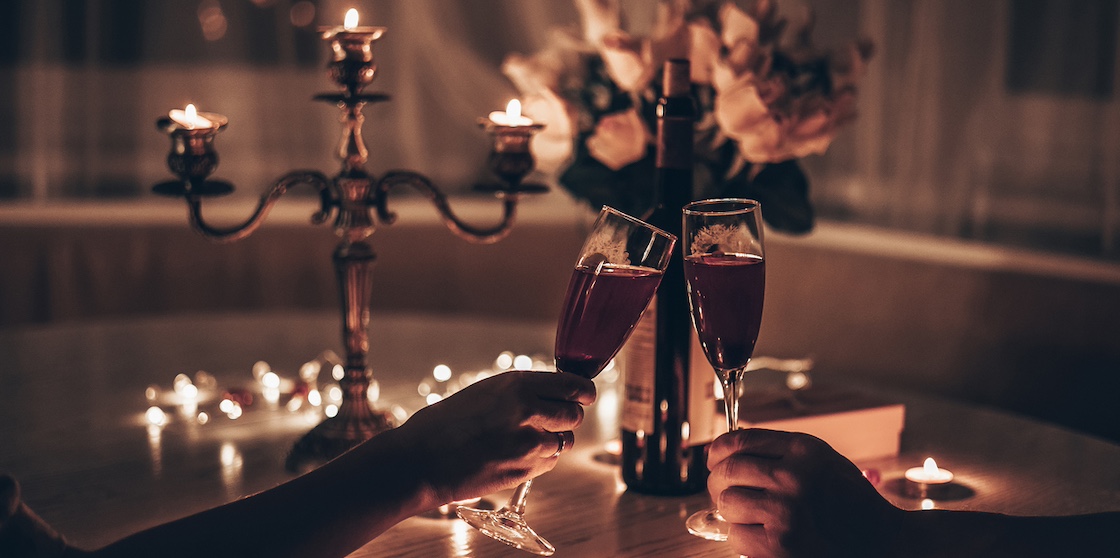 Hands man and woman holding glasses of wine having romantic candlelight dinner at table at home. Hands man and woman holding glass of wine. Concept of Valentine's day or Candlelight date at night.