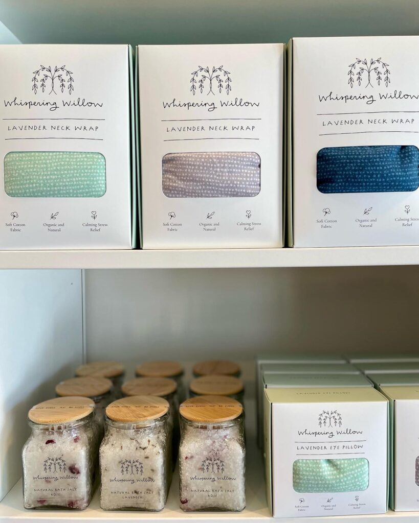 self-care items on a shelf from wallflower mercantile including bath. salts, eye pillows, and neck wraps