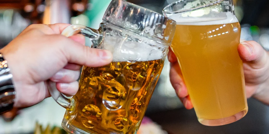 Two friends hands clinking glasses of craft beer at the pub or bar