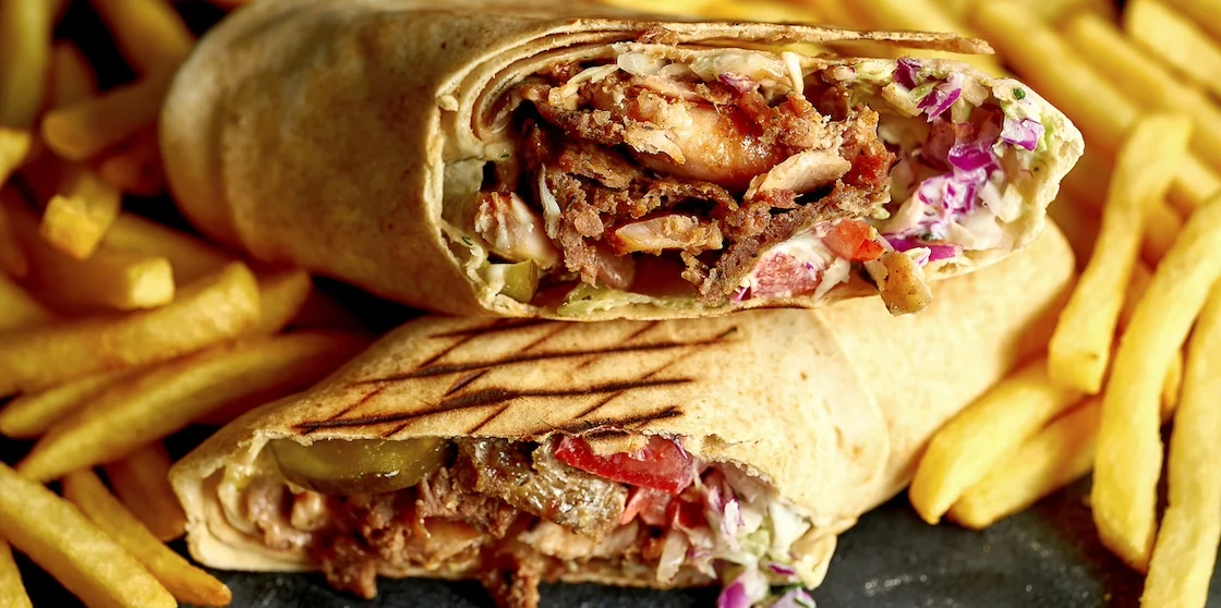 Big shawarma with vegetables and meat on a dark background with fries. Close up, selective focus