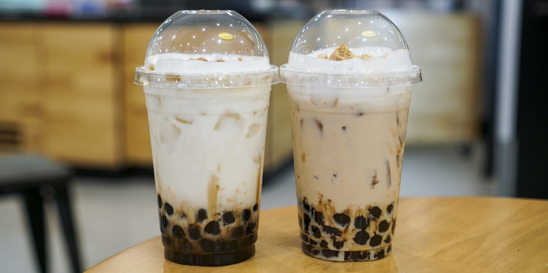 A plastic cup of fresh milk and milk tea with brown sugar boba/bubble on wooden table.