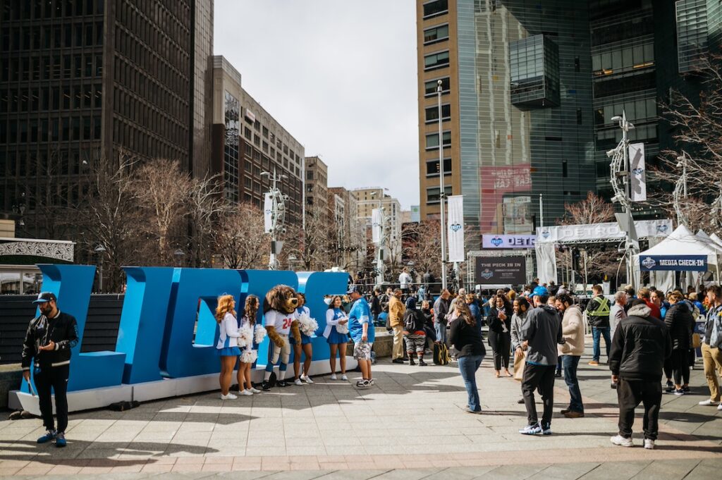 crowd surround a lions sign in the downtown detroit area posting with cheerleeders