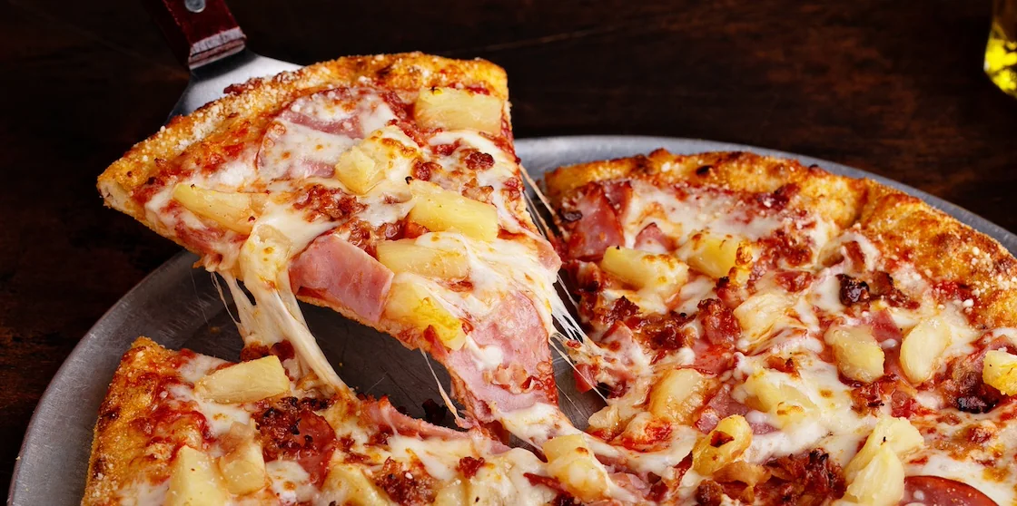 Hawaiian pizza with ham and pineapple cut into slices, cheese pull