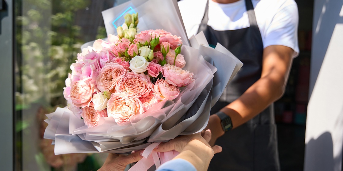 Woman buyer takes a beautifully formed bouquet of flowers in colored wrapping paper