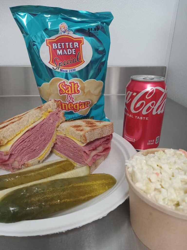 mid eight sandwich shop spread with sandwiches, chips, pickle, pop, and cole slaw