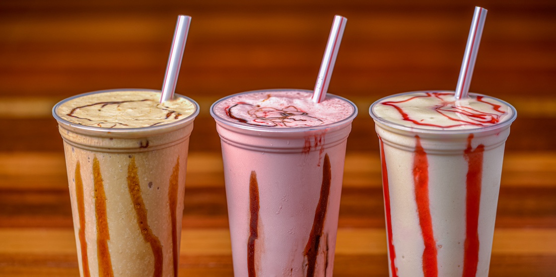 Milkshakes in plastic cups and straws on a dark wooden table.