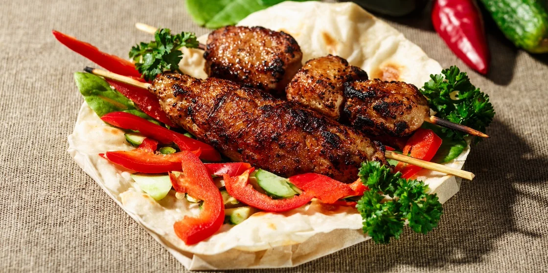 Shish kofte (kofta kebab) with vegetables and herbs on naan or lavash or pita flatbread - halal