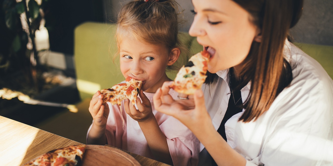 Happy mother and daughter eat pizza in a cafe and having fun - kid menu