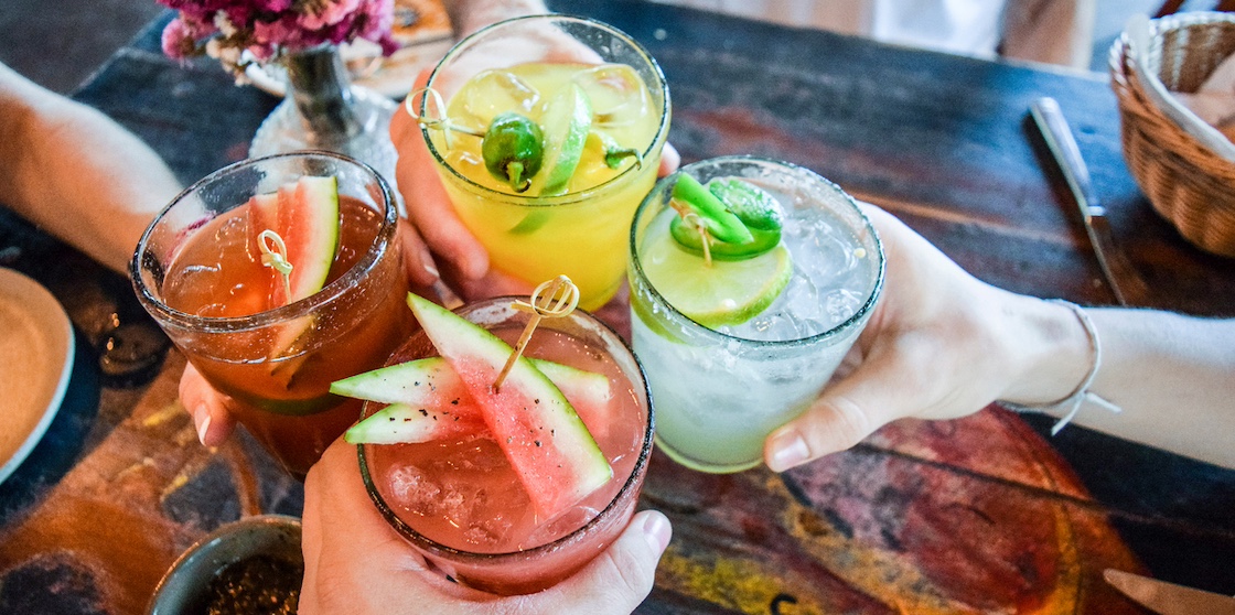 Friends toasting, saying cheers holding tropical blended melon fruit margaritas. Watermelon and passionfruit drinks.