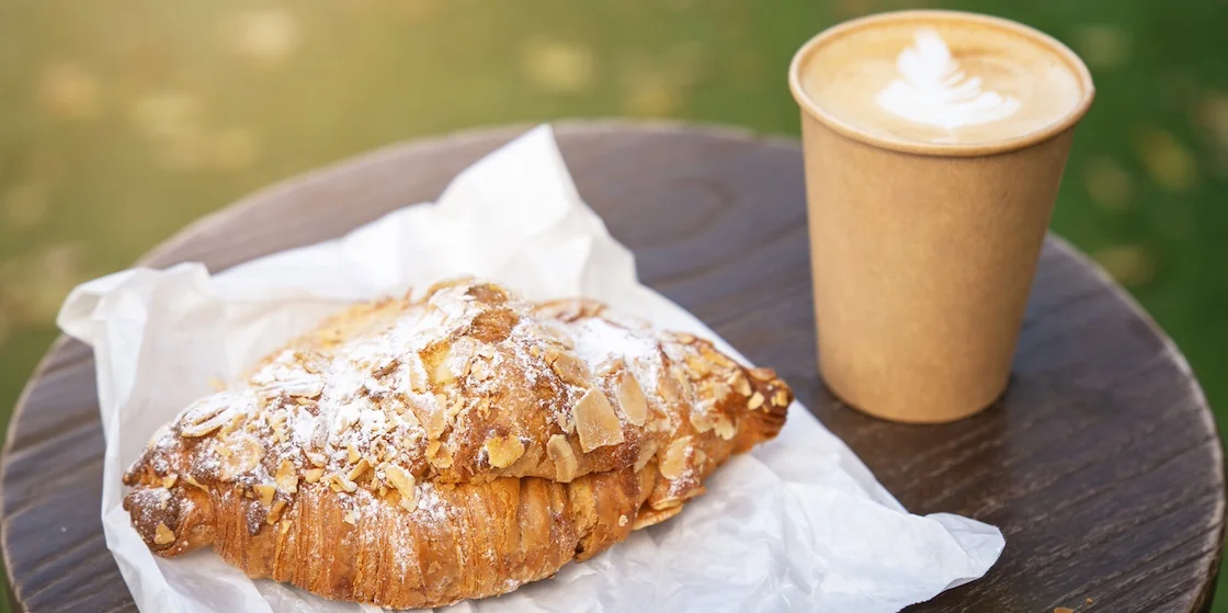 Cappuccino coffee in a paper cup and a bun sprinkled with nuts Breakfast at an outdoor café