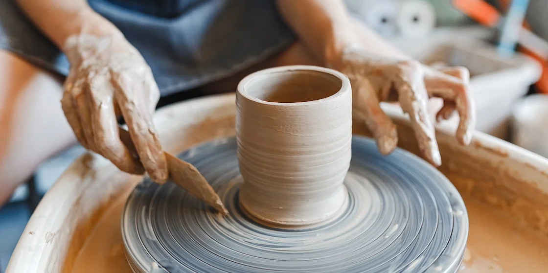 Top view of hands with clay making of a ceramic pot on the pottery wheel, hobby and leisure classes