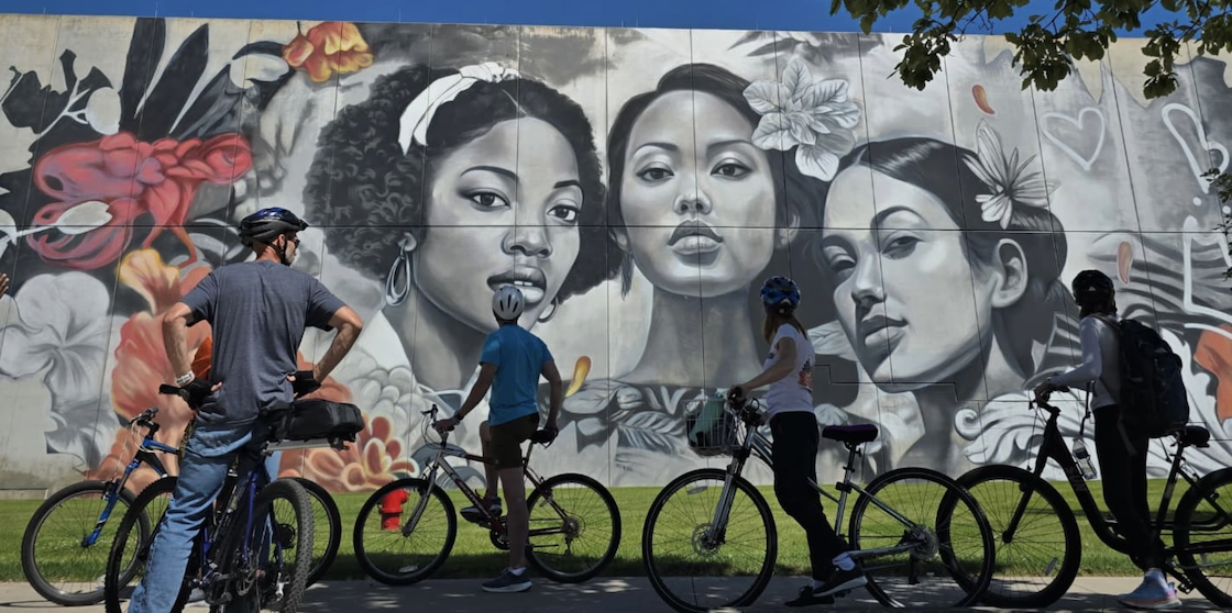 Bike riders stopped in front of a mural while touring