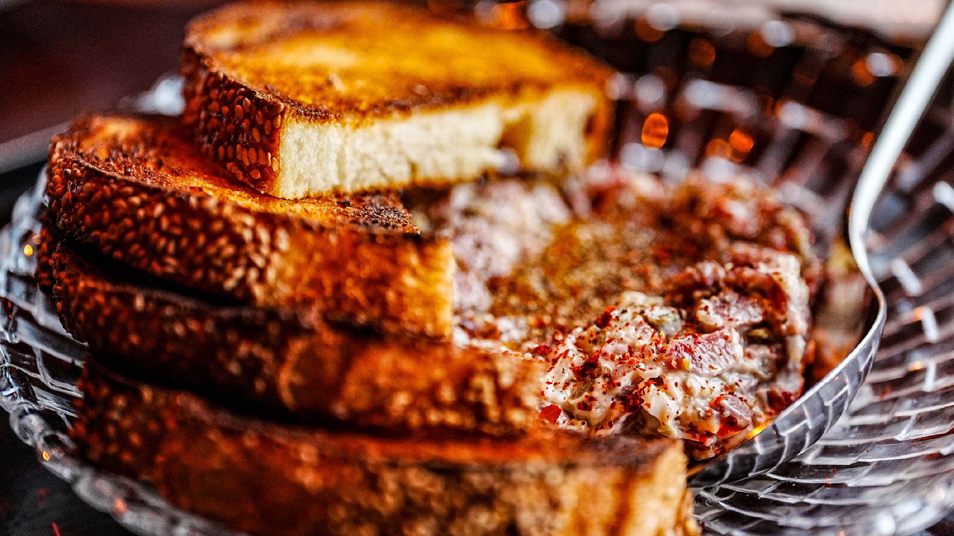 Close-up of toasted sesame-crusted bread slices served alongside a seasoned meat dish in a metal basket at Wilder's