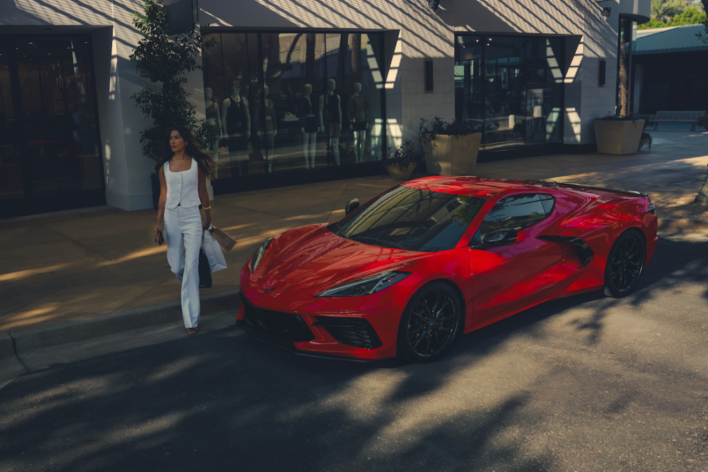 Woman with shopping bags walking around the front of a red Corvette Stingray
